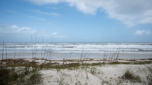 A beach with waves, sand, and sparse vegetation. - Coquina B101 Ground-Floor Coastal Condo (Saint Augustine)