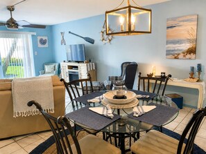 A dining area with a round glass table, chairs, and a chandelier. - Ground-Floor Oceanfront Condo | Steps to Beach (Saint Augustine)