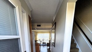 A hallway with a door on the left, a staircase on the right, and a living area in the background. - Oceanview Townhouse with Pool & Balcony Access (Saint Augustine)