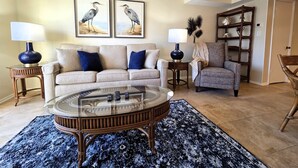 A living room with a beige sofa, two blue lamps, a glass coffee table, and a patterned rug. There are two framed bird paintings on the wall. - Oceanview Townhouse with Pool & Balcony Access (Saint Augustine)