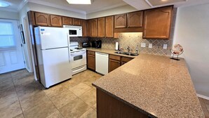 A kitchen with wooden cabinets, a white refrigerator, a stove, a microwave, and a dishwasher. - Oceanview Townhouse with Pool & Balcony Access (Saint Augustine)