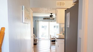 Um corredor com piso ladrilhado que leva a uma área de cozinha, com geladeira, mesa de jantar e uma cadeira.
