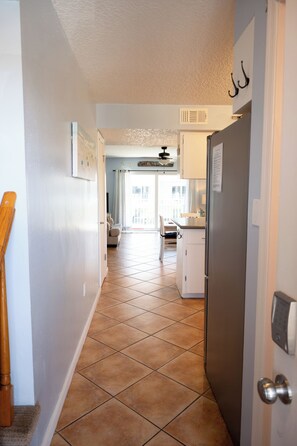 A hallway with a tiled floor leading to a kitchen area with a refrigerator, a dining table, and a chair.
