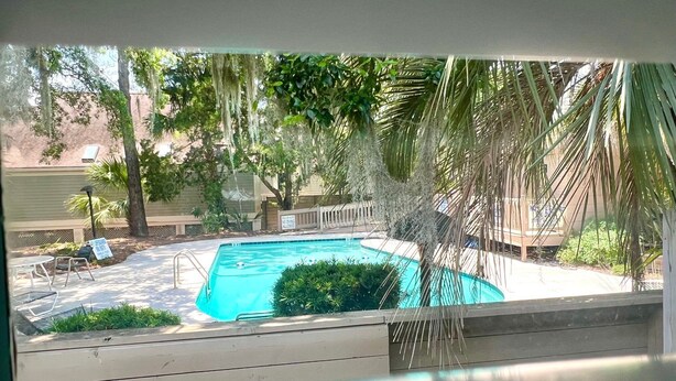 A view of a swimming pool with a wooden deck, surrounded by palm trees and a fence. - The Pearl by Sandpiper | Near Beach (Seabrook Island)