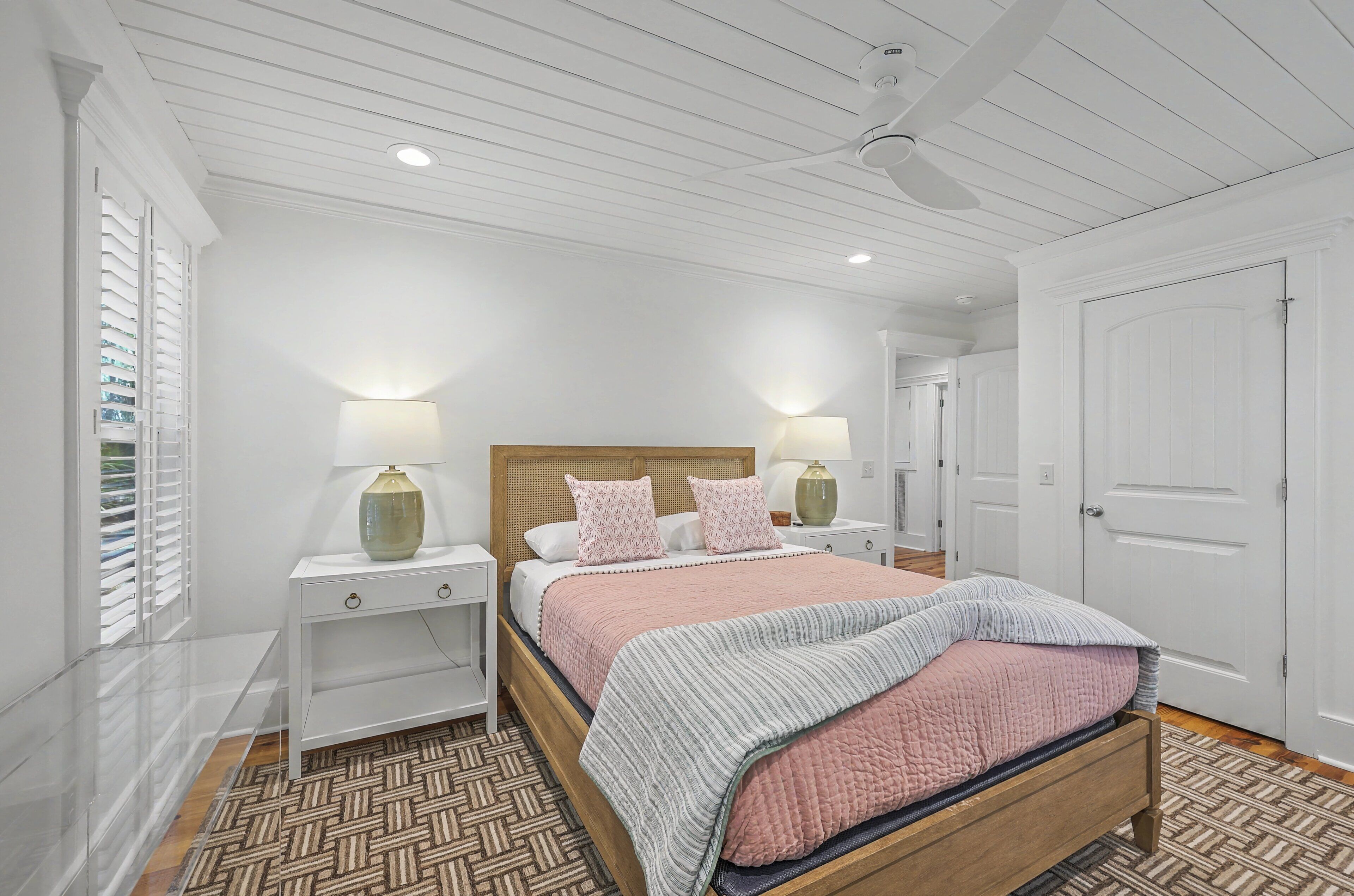 A bedroom with a wooden bed, white nightstands, a ceiling fan, and a patterned rug.