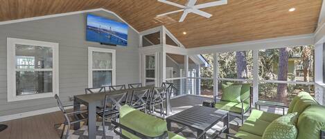 A covered patio with a ceiling fan, a dining table with chairs, and a sofa with cushions.