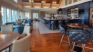 A spacious bar area with high ceilings and large windows, a bar counter with stools, and a seating area with tables and chairs. - Mystic Pines by Sandpiper | Near Beach (Seabrook Island)