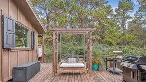 Eine Holzterrasse mit Schaukelstuhl, Grill und einer Topfpflanze.