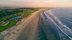 Eine Luftaufnahme einer Küstenregion mit einem langen Sandstrand, einem Golfplatz und einem Gewässer.