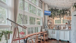A rustic kitchen with wooden bar stools, a large window, and a hanging fern. - Escape to The Hummingbird Treehouse, a luxury retreat. Pet friendly (Wadmalaw Island)