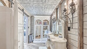 Un pasillo estrecho con un espejo antiguo, una tocador blanca con espejo y suelo de madera.