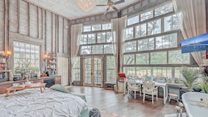 Una habitación amplia con ventanas grandes, una cama, un escritorio y un televisor.