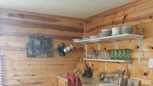 Un intérieur en bois avec un coin cuisine comprenant une table en bois, des chaises, un torchon rouge et un petit îlot avec un évier et des ustensiles.