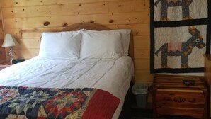 Une pièce aux murs lambrissés, comprenant un lit, une courtepointe, une décoration murale et une table de chevet.