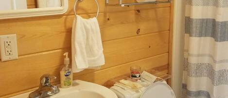 A bathroom with a wooden wall, a sink, a toilet, a towel rack, and a shower curtain.