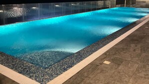 Una piscina con acqua cristallina, circondata da un solarium piastrellato e un'area vetrata.