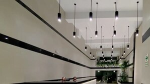 Un'ampia hall moderna con una reception, diverse lampade a sospensione e un pavimento pulito rivestito di piastrelle.