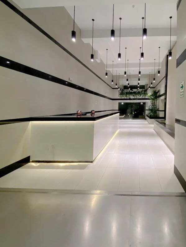 Un hall d’entrée spacieux et moderne, doté d’un comptoir de réception, de plusieurs luminaires suspendus et d ’un sol carrelé et impeccable.