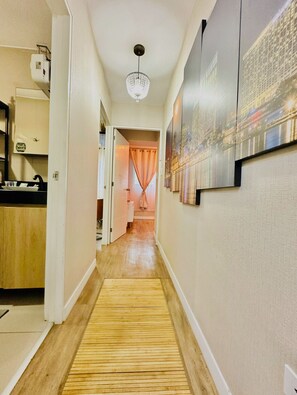 A hallway with a wooden floor, a ceiling light, and a door leading to a room with a pink curtain.