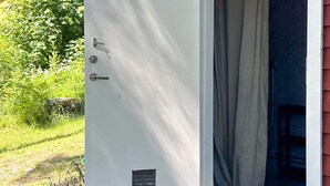 Een witte deur met een slot en een klein ventilatie rooster, leidend naar een kamer met een gordijn.