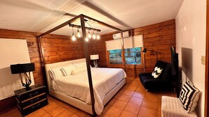 Une chambre à coucher avec un lit à baldaquin, une table de chevet, une lampe, un téléviseur et une fenêtre donnant sur des arbres.