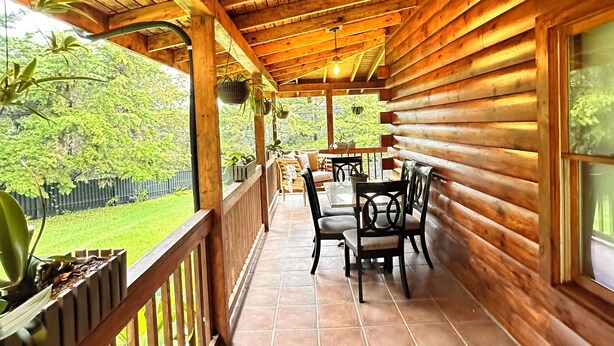 Une cabane en rondins de bois dotée d’un patio couvert comprenant une table et des chaises, le tout entouré d’une balustrade en bois et de plantes en pot.
