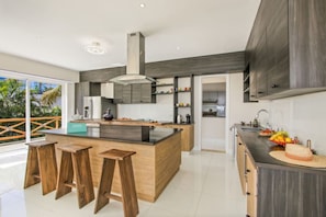 Une cuisine moderne dotée d’un îlot central, de tabourets en bois et offrant une vue sur l’extérieur.