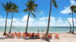 A beach with palm trees and orange lounge chairs. - Okyanus: Spectacular oceanview estate w/ pool, Jacuzzi, full staff & golf cart (Punta Cana)