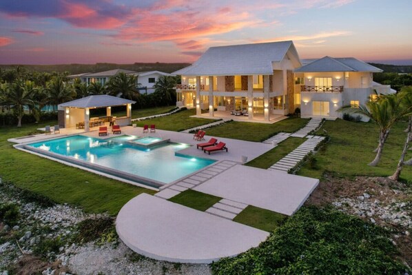 A modern two-story house with a swimming pool, outdoor seating, and a well-maintained lawn.