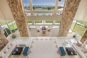 A spacious lobby with a high ceiling, large windows, and a view of a pool and greenery. - Okyanus: Spectacular oceanview estate w/ pool, Jacuzzi, full staff & golf cart (Punta Cana)