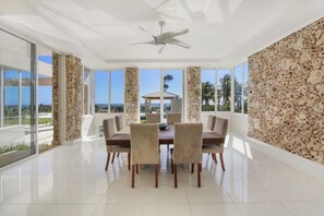 A spacious dining area with a high ceiling fan, large windows, and a view of the ocean.