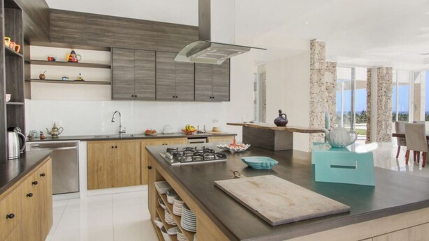 A modern kitchen with a central island, built-in cabinets, and a large window offering a view. - Okyanus: Spectacular oceanview estate w/ pool, Jacuzzi, full staff & golf cart (Punta Cana)