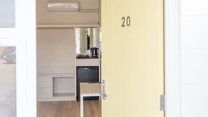 A hotel room with a yellow door marked '20', a white wardrobe, a small kitchenette with a coffee maker, and a mirror above the counter. - Sunnyside Motel (Port Broughton)