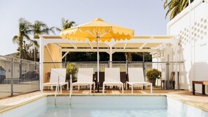 A pool area with a covered seating area, lounge chairs, and a yellow umbrella. - Sunnyside Motel (Port Broughton)