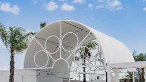 A modern building with a unique circular entrance design, palm trees, and a parking area. - Sunnyside Motel (Port Broughton)