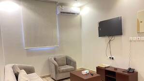 Una habitación moderna con sofá, sillón y una mesita de centro. Hay un televisor de pantalla plana montado en la pared y un mueble de madera con un teléfono.
