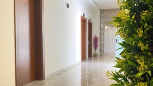 Un pasillo con piso de mármol, puertas de madera y una planta en maceta con flores amarillas.