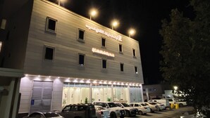 Un edificio con múltiples ventanas y un letrero en idioma extranjero. Varias automóviles están estacionadas adelante.