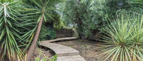 A wooden pathway leading through a garden with various plants and trees.
