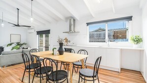 Une cuisine moderne avec une table en bois, des chaises noires et une grande fenêtre donnant sur une maison.