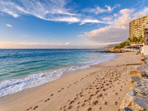 Un hotel frente a la playa con arena, vista al océano y un muro de piedra.