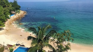 A beach with clear turquoise water, a sandy shore, and a pool area with umbrellas. - Beachfront Oasis with a View - Puerto Vallarta (Puerto Vallarta)