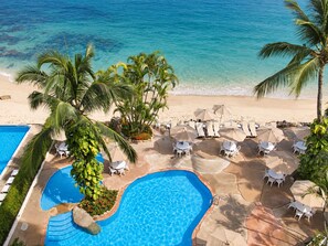 Une piscine d’un complexe hôtelier offrant une vue dégagée sur l’océan, entourée de palmiers et de chaises longues.