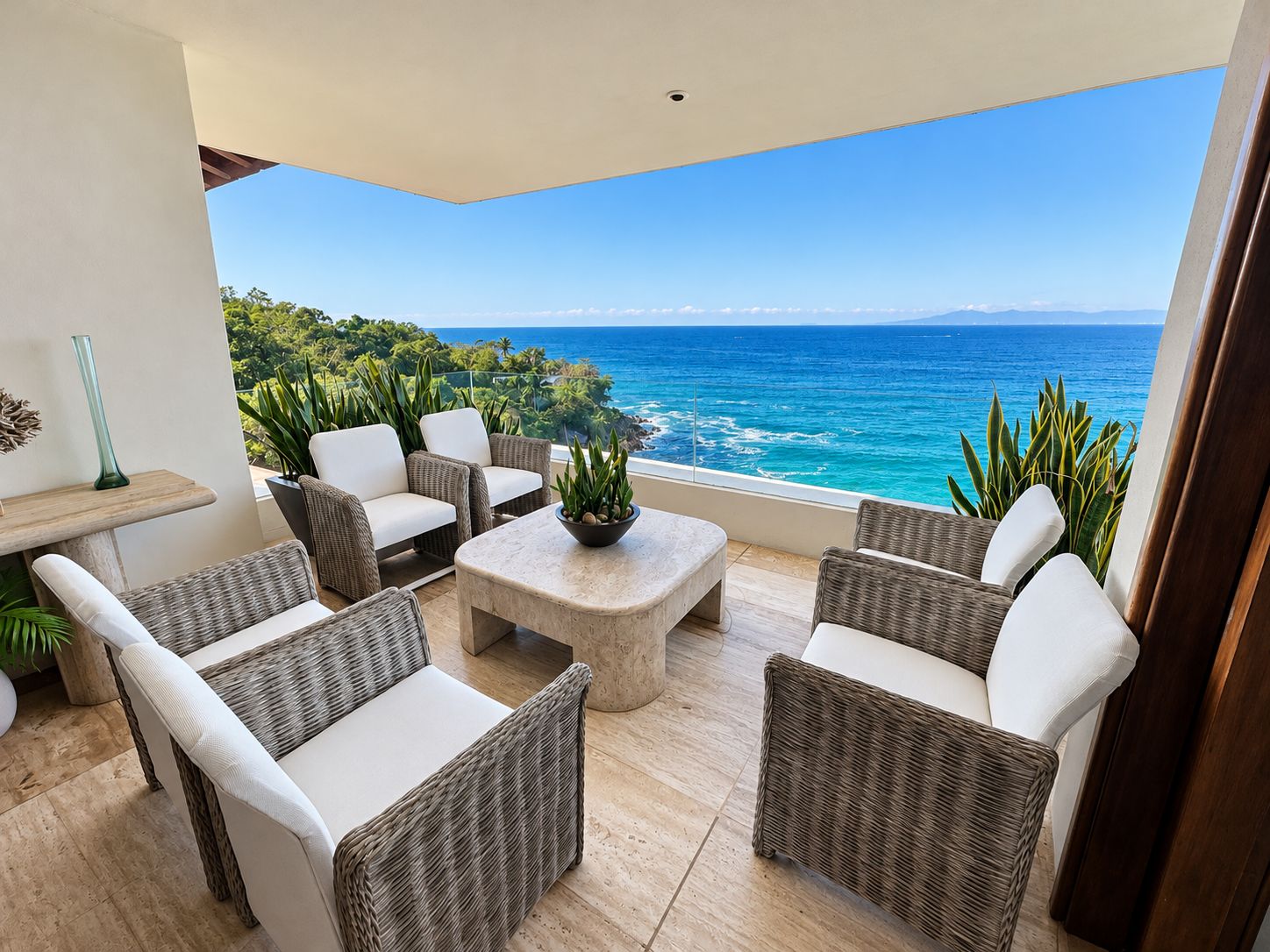 A balcony with wicker furniture, a small table, and a view of the ocean.