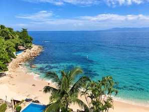 A beach with clear turquoise water, a sandy shore, and palm trees.