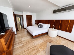 Una habitación de hotel moderna con una cama grande, un televisor sobre un tocador de madera y una mesita de noche redonda con una lámpara.