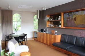 A modern kitchen with wooden cabinets, a dining area with a table and chairs, a sofa, and a large window.