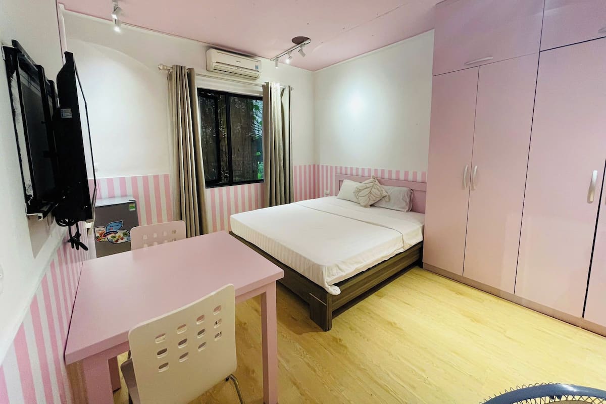 A bedroom with a bed, a desk, a wardrobe, and an air conditioning unit.