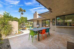 Relax in a serene outdoor space with a patio table, chairs, and a hanging chair, surrounded by lush plants and a modern design.