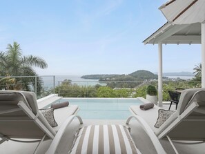 Ein Poolbereich mit zwei Liegestühlen und Blick auf das Meer und die Hügel.